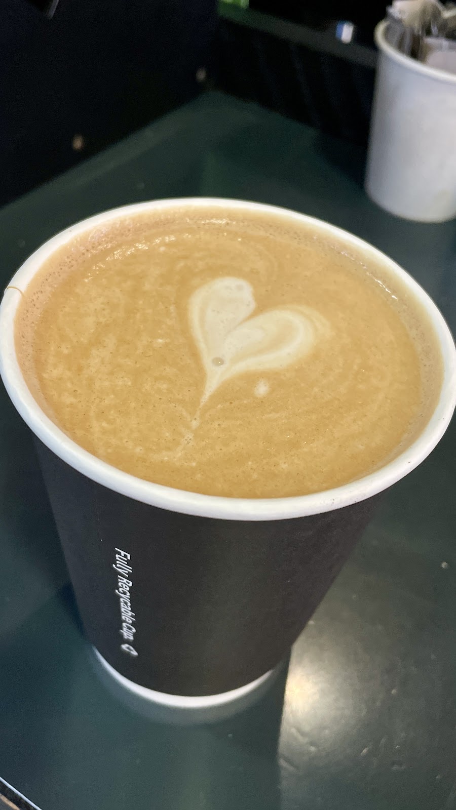 A flat white in a dark cup with a white heart poured in the crema