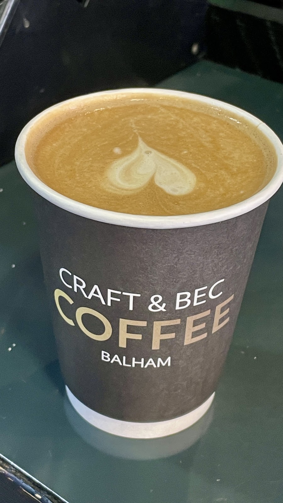 A tall coffee on the green counter with a heart poured in the foam