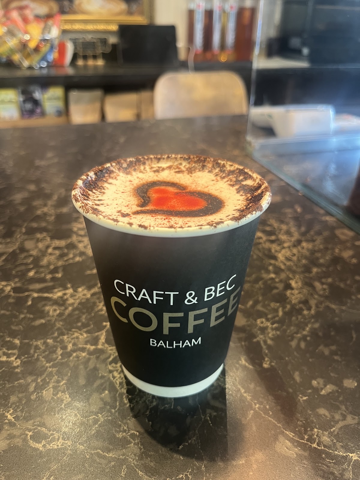 A takeaway coffee on a dark marble counter, chocolate-dusted heart in the foam